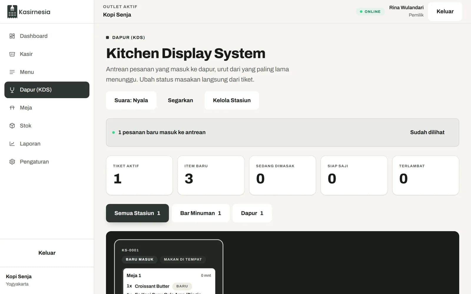 Layar Kitchen Display dengan tiket pesanan Meja 1 berisi Es Kopi Susu Gula Aren, Croissant Butter, dan Americano